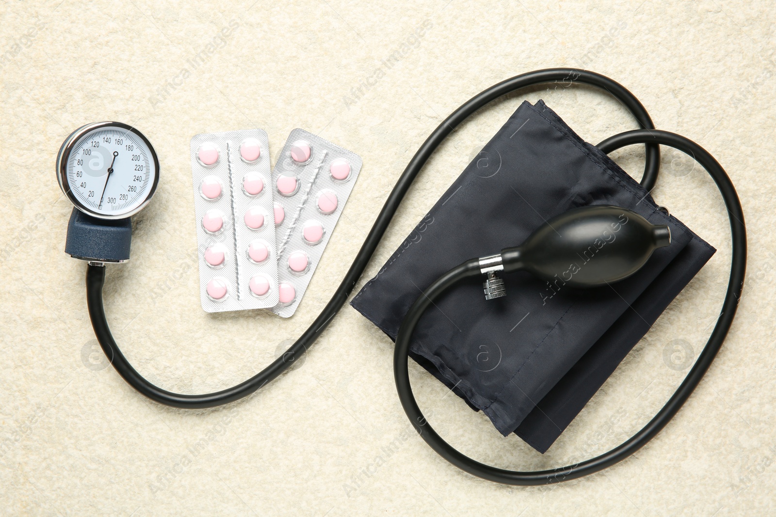 Photo of Blood pressure measuring device and pills on light textured background, top view