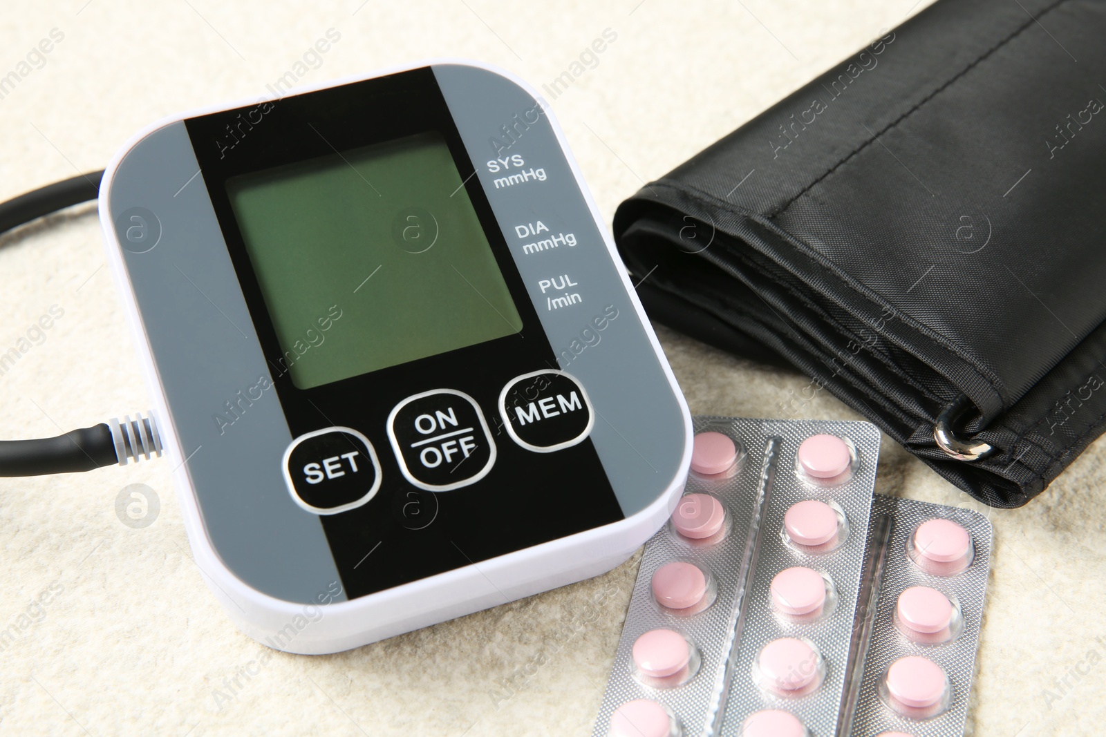 Photo of Blood pressure measuring device and pills on light textured background, closeup