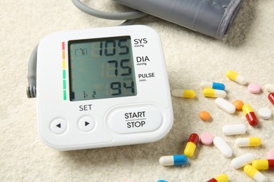 Photo of Blood pressure measuring device and pills on light textured background, closeup