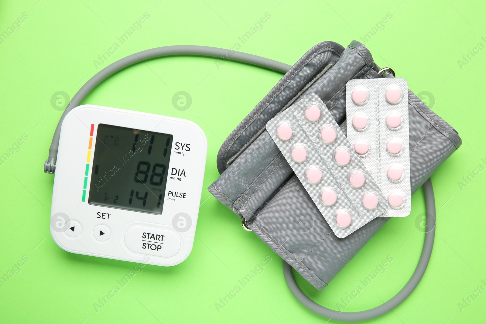 Photo of Blood pressure measuring device and pills on green background, top view