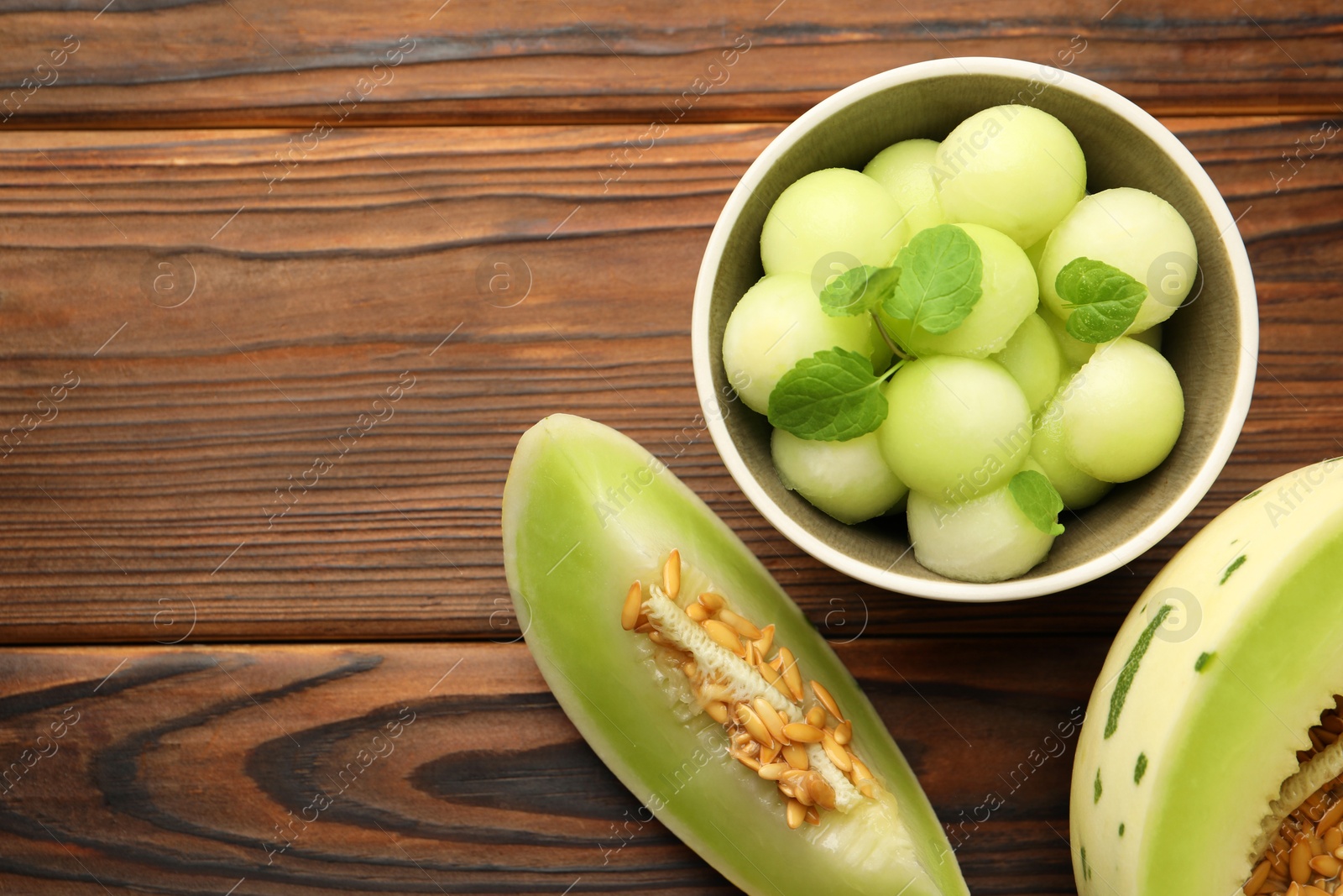 Photo of Melon balls in bowl and fresh fruit on wooden table, flat lay. Space for text