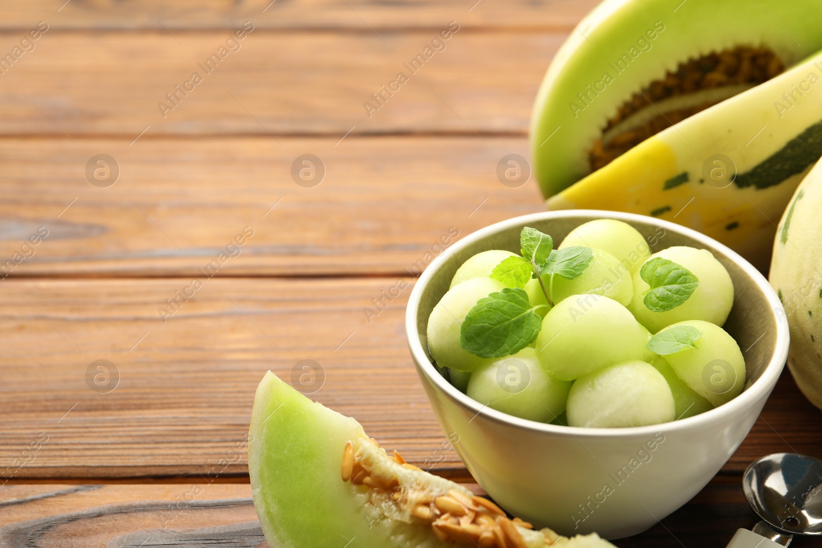 Photo of Melon balls in bowl and fresh fruit on wooden table. Space for text