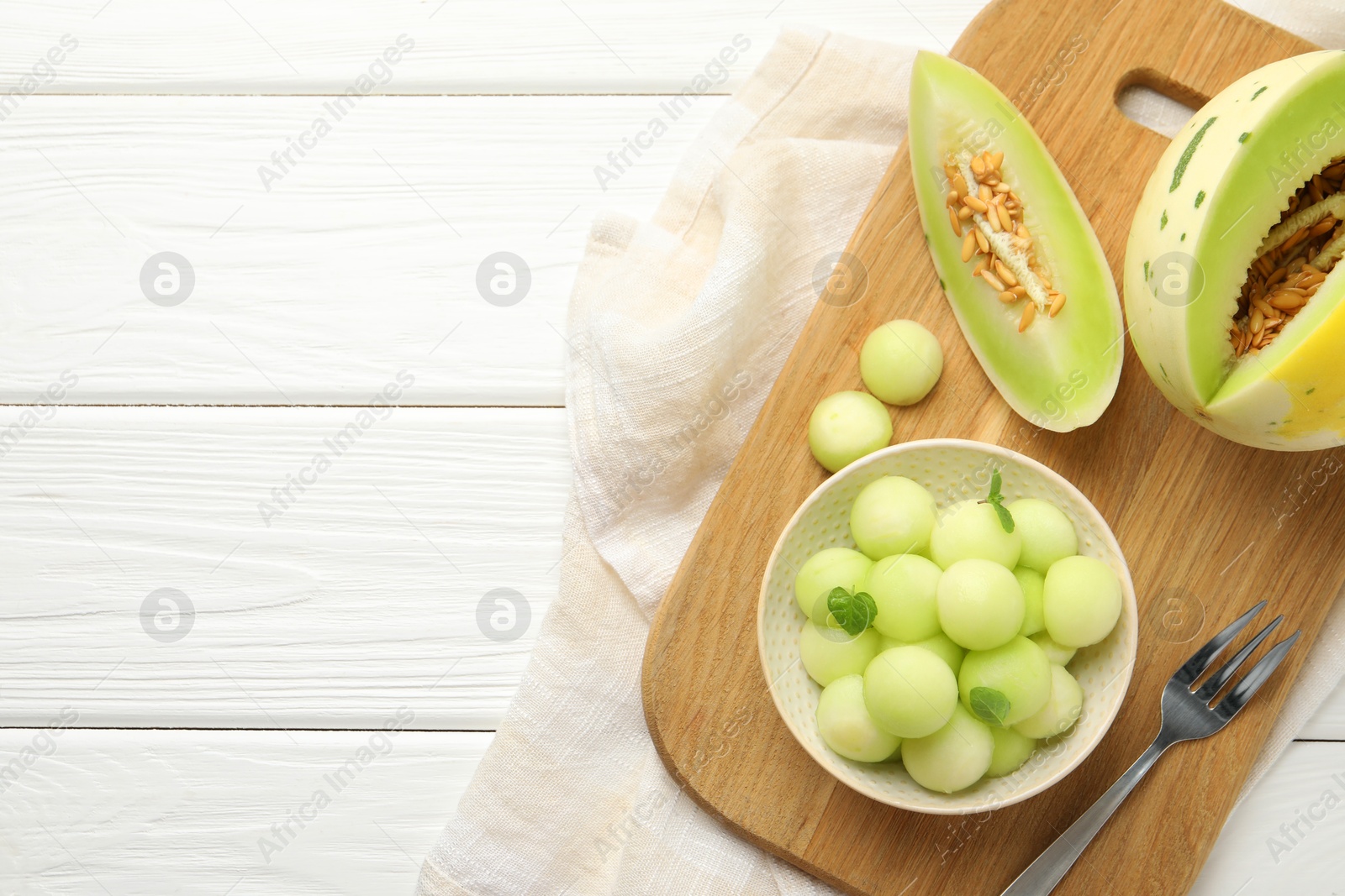 Photo of Melon balls in bowl and fresh fruit on white wooden table, top view. Space for text