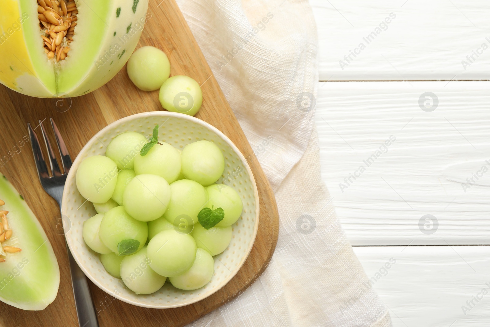 Photo of Melon balls in bowl and fresh fruit on white wooden table, top view. Space for text