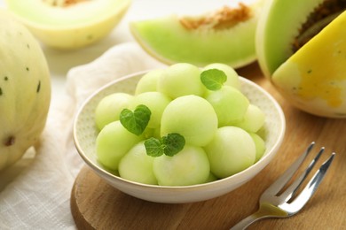 Photo of Melon balls in bowl and fresh fruit on wooden table, closeup