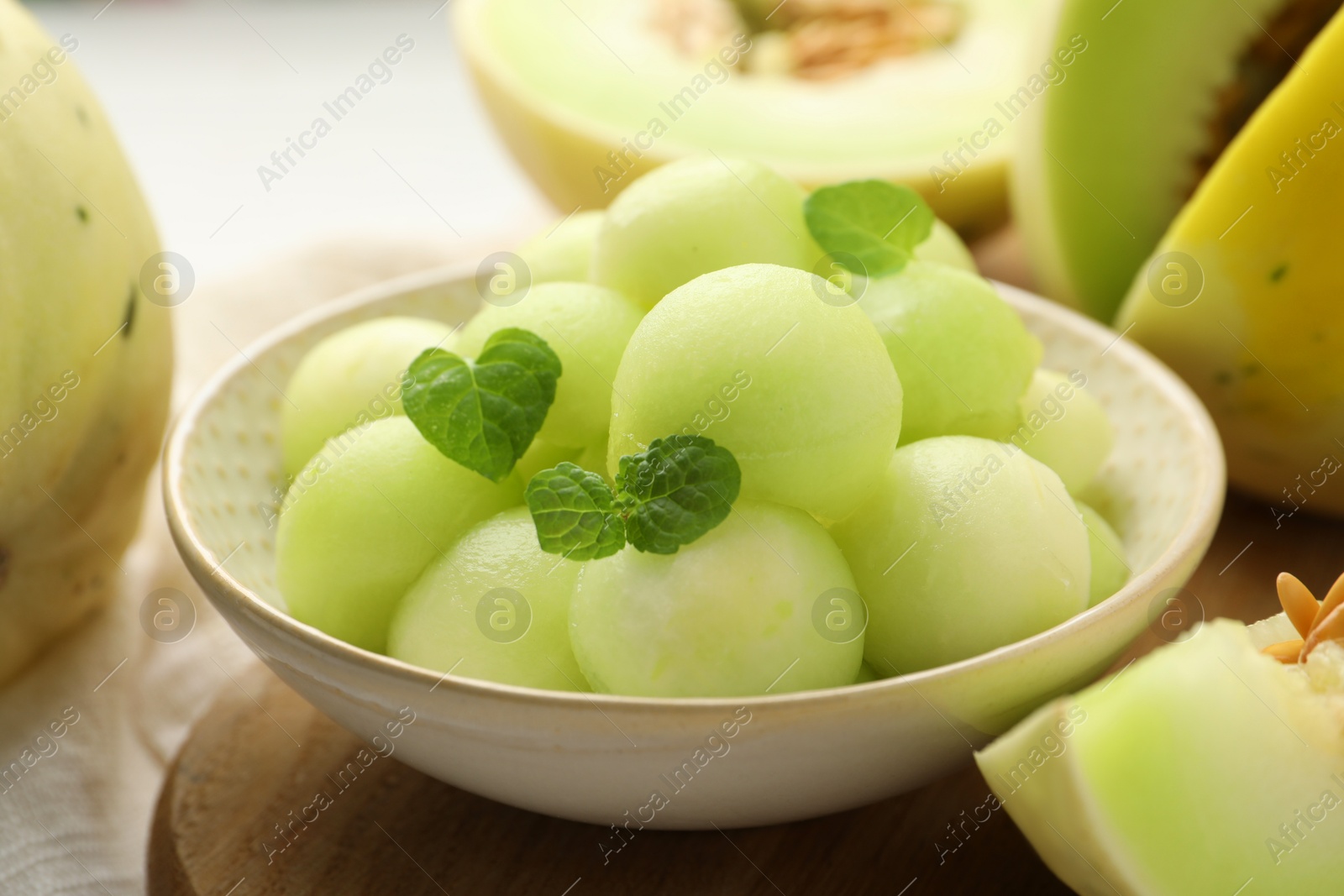 Photo of Melon balls in bowl and fresh fruit on wooden table, closeup