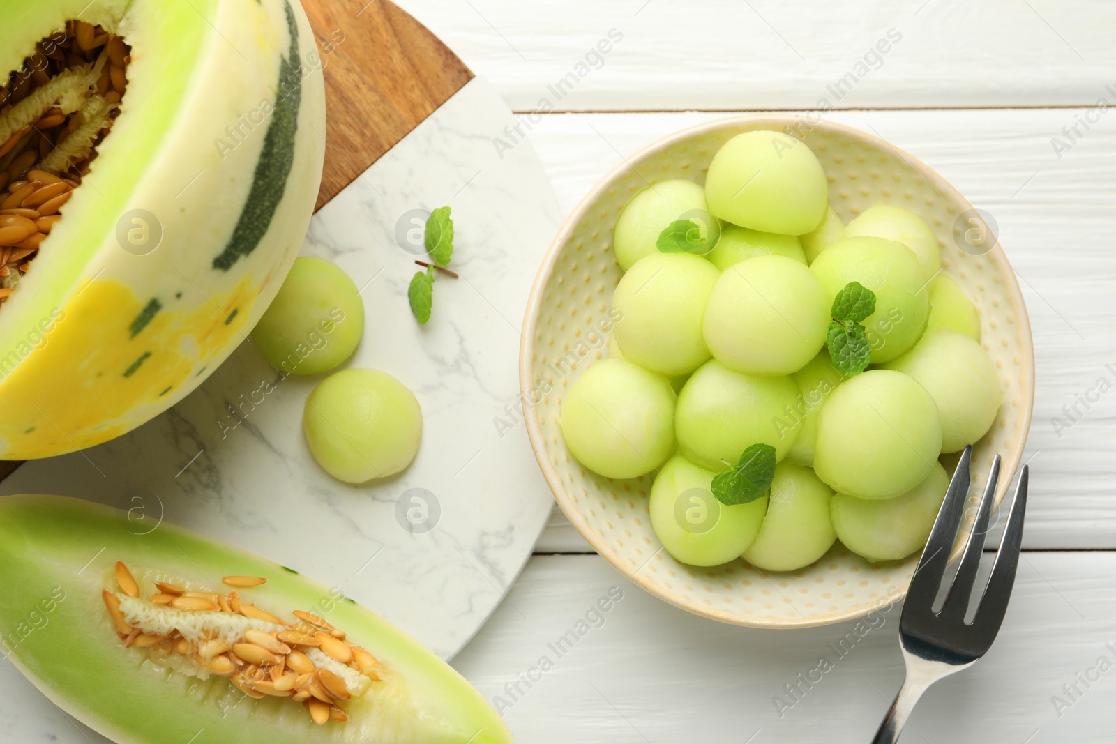 Photo of Melon balls in bowl and fresh fruit on white wooden table, flat lay