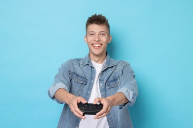 Happy young man playing video games with controller on light blue background