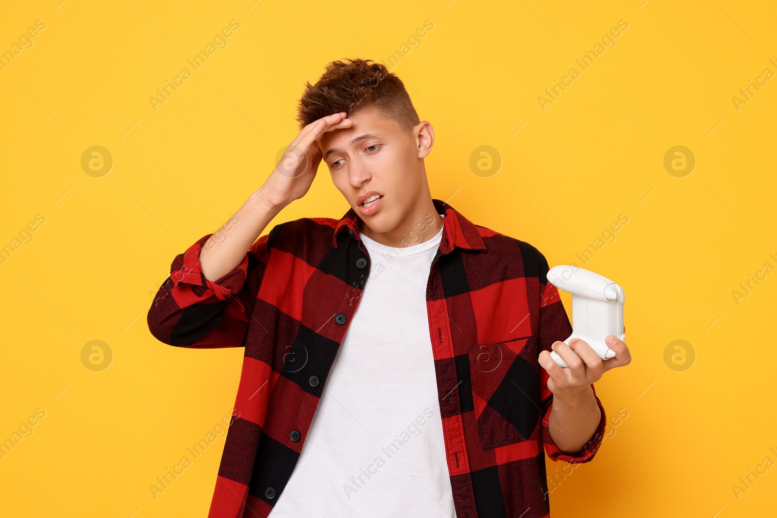 Photo of Unhappy young man with controller on orange background