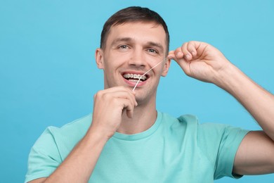 Photo of Man with braces cleaning teeth using dental floss on light blue background