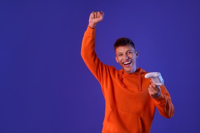 Happy young man with controller on violet background, space for text