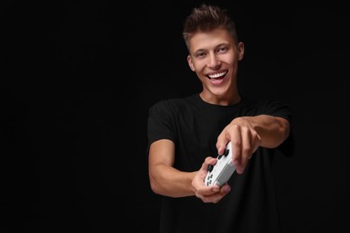 Happy young man playing video games with controller on black background, space for text