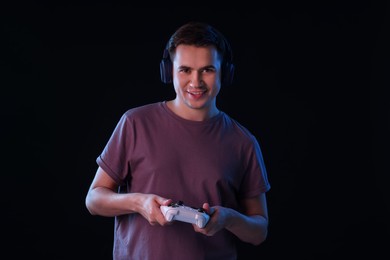 Young man in headphones playing video games with controller on black background