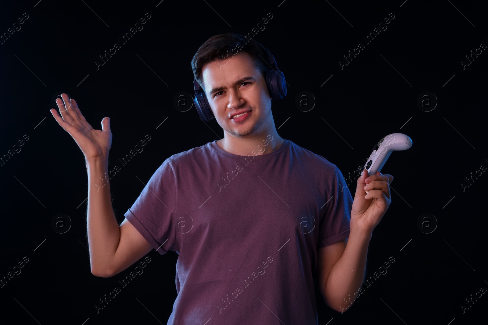 Photo of Young man in headphones playing video games with controller on black background