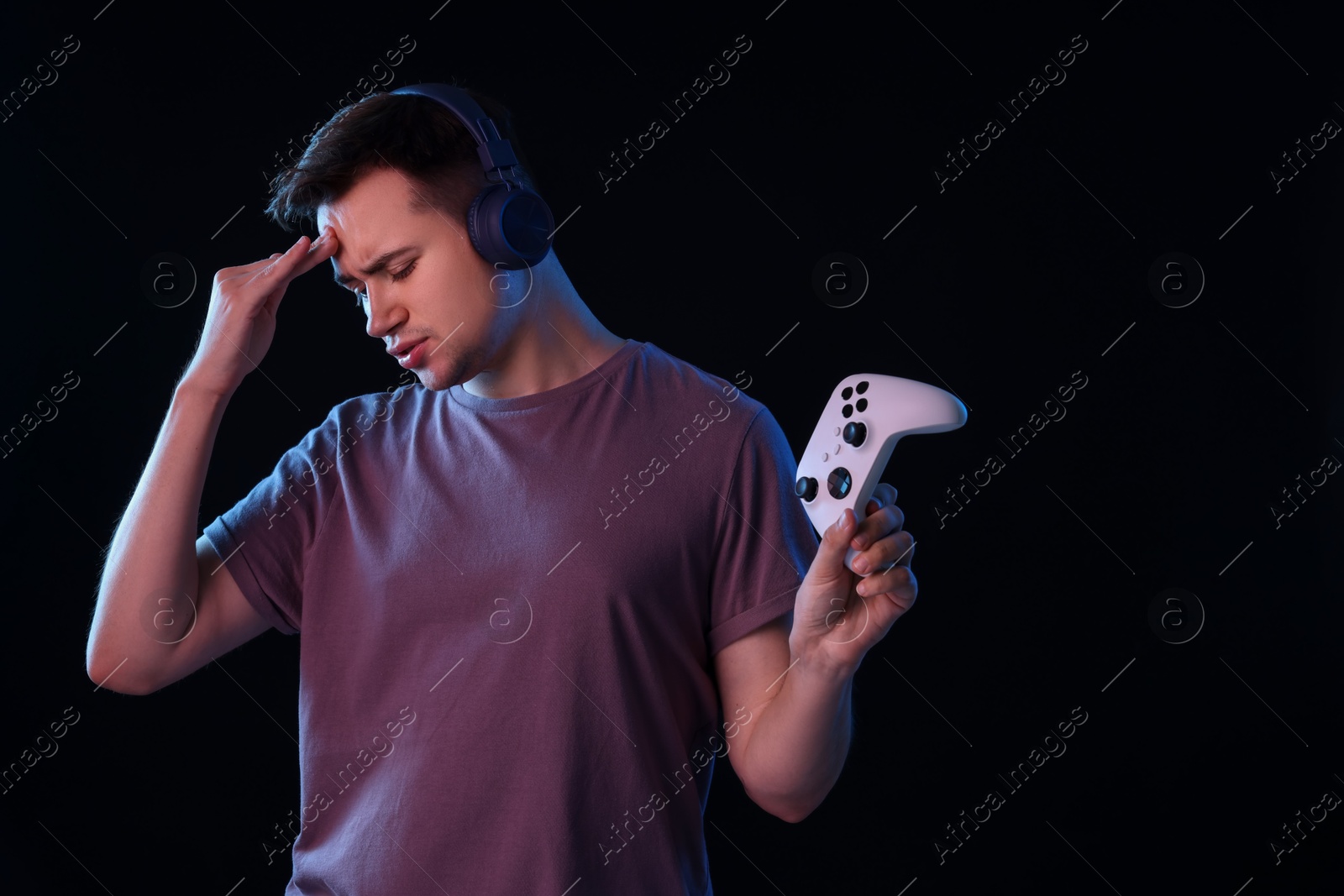 Photo of Unhappy young man in headphones playing video games with controller on black background