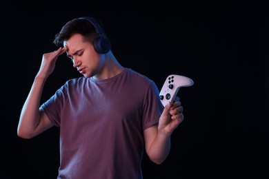 Photo of Unhappy young man in headphones playing video games with controller on black background