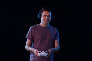 Young man in headphones playing video games with controller on black background