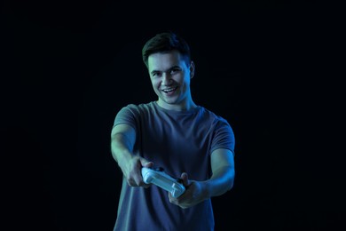 Happy young man playing video games with controller on black background