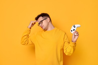 Unhappy young man with controller on orange background