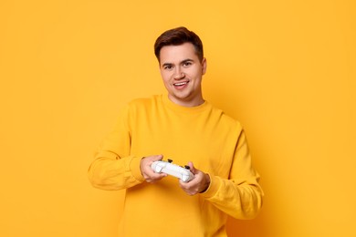 Happy young man playing video games with controller on orange background