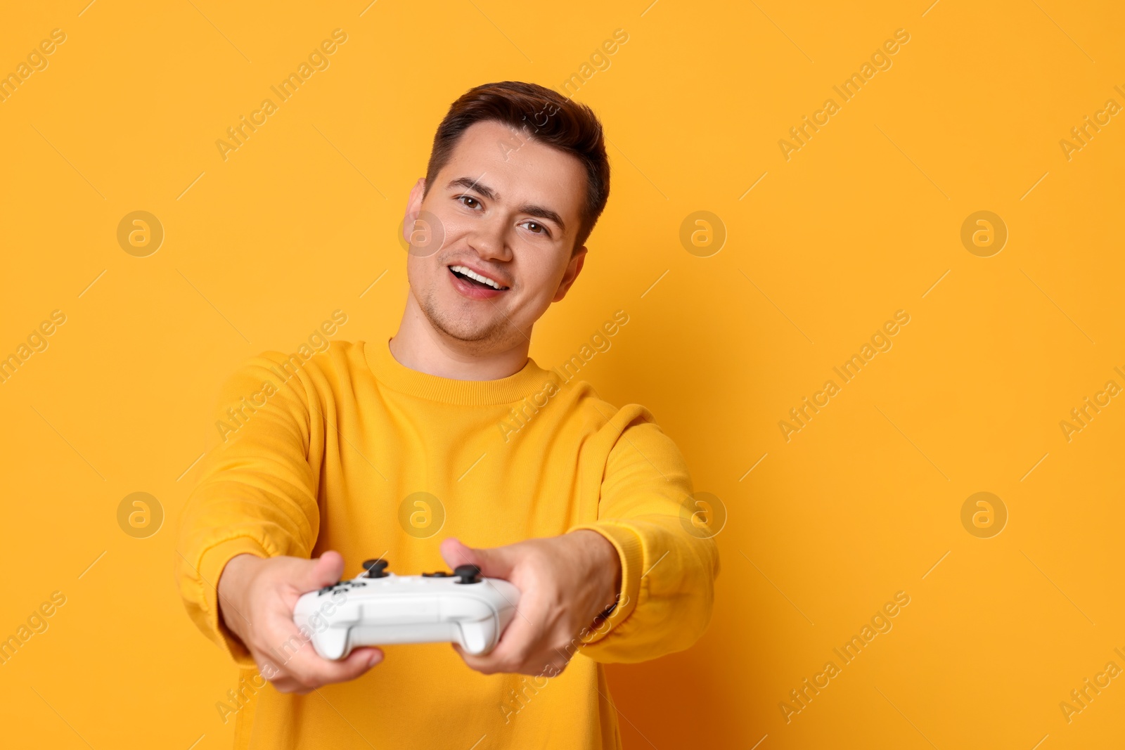 Photo of Happy young man playing video games with controller on orange background, space for text