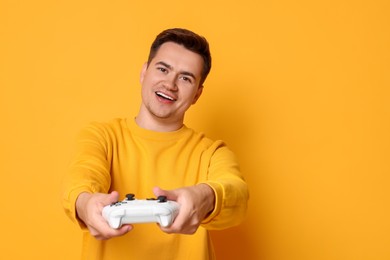 Happy young man playing video games with controller on orange background, space for text