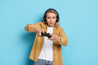 Woman in headphones playing video games with controller on light blue background