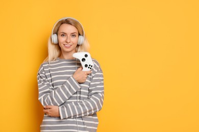 Happy woman in headphones with controller on orange background, space for text