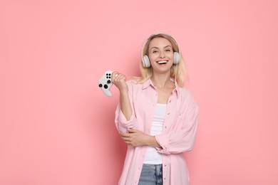 Photo of Happy woman in headphones with controller on pink background