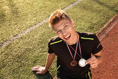 Photo of Happy winner with different medals sitting at stadium on sunny day. Space for text