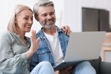 Photo of Happy middle aged couple having video chat via laptop on sofa indoors