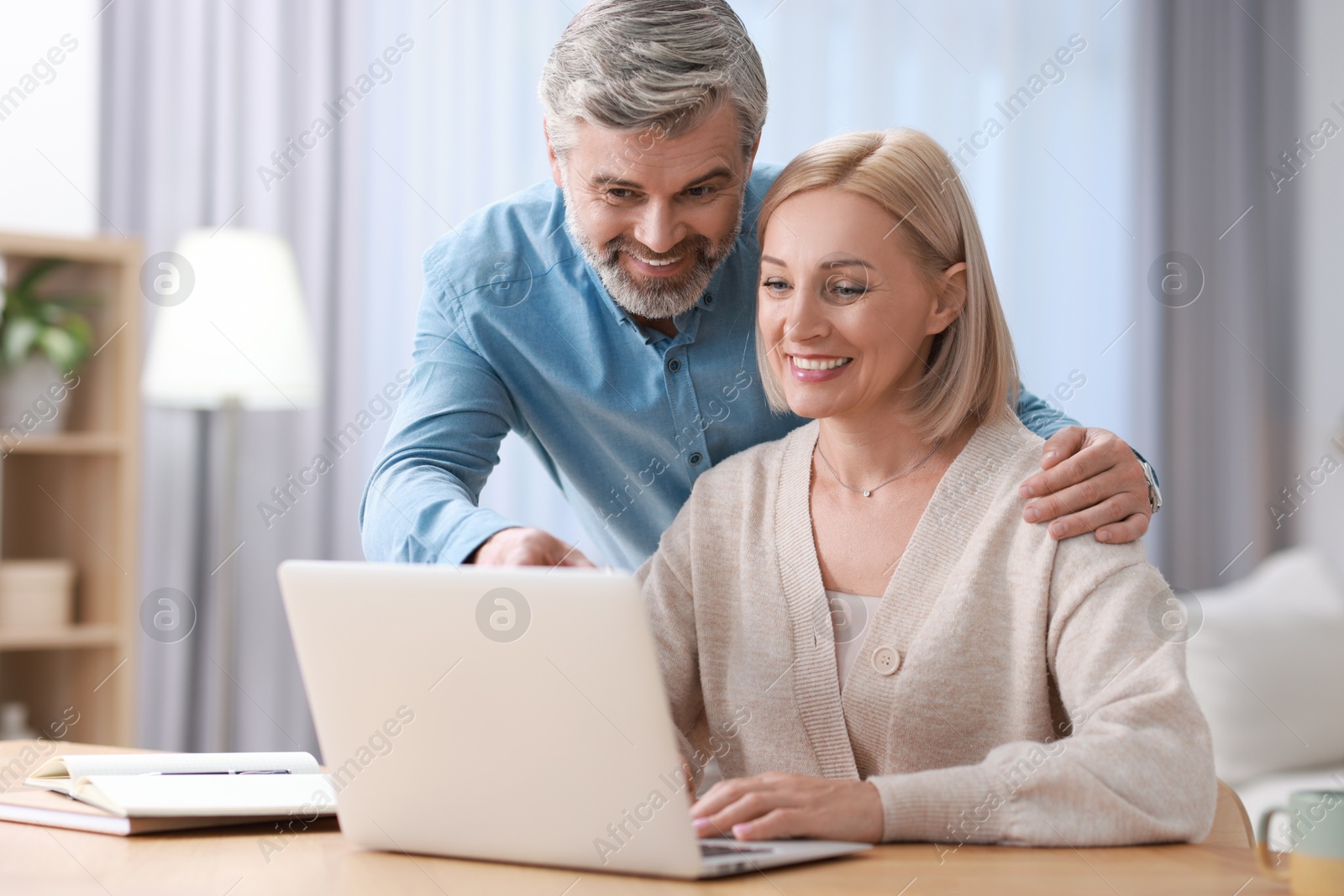 Photo of Happy middle aged couple working with laptop at table indoors