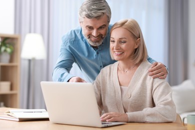 Happy middle aged couple working with laptop at table indoors