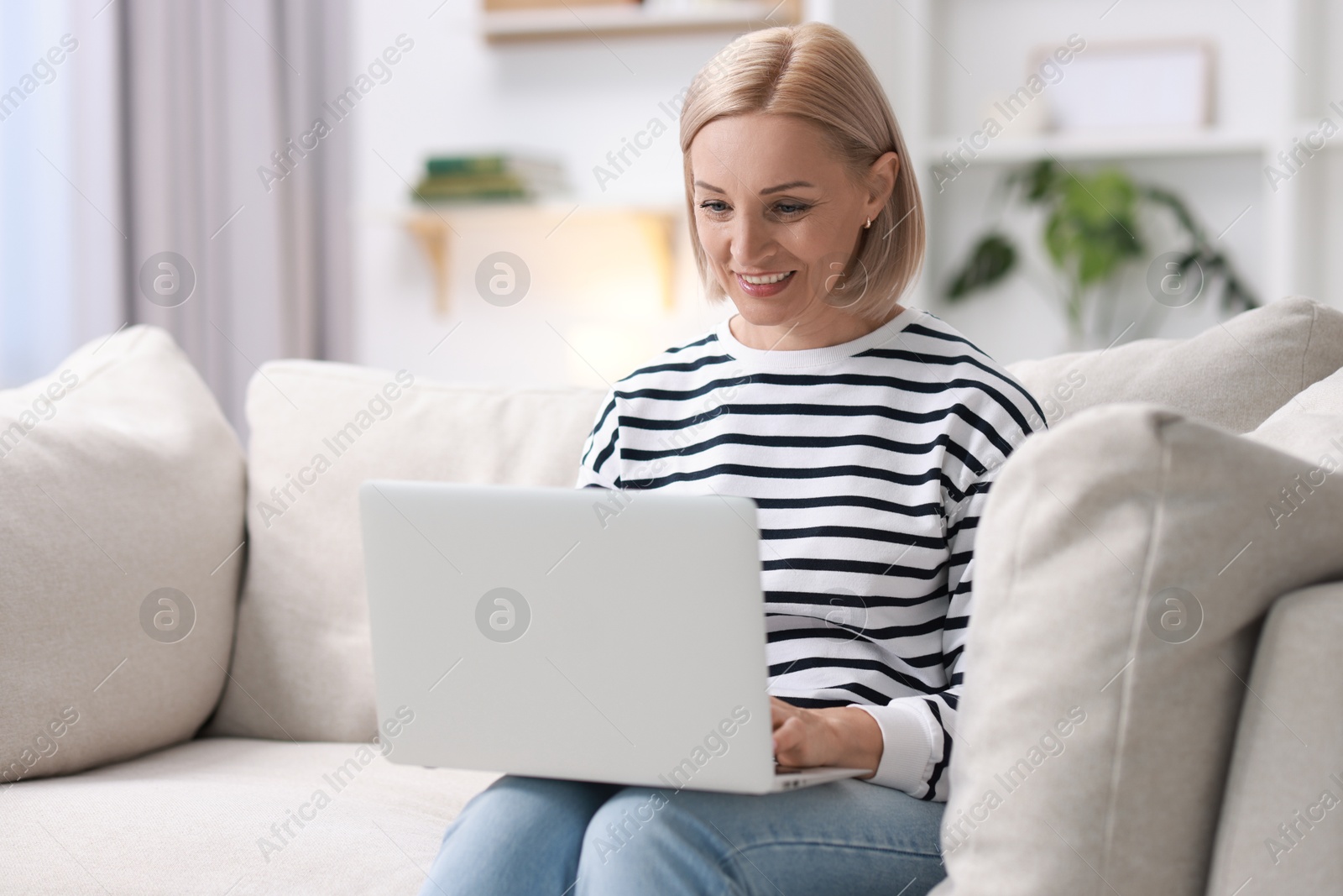 Photo of Happy middle aged woman using laptop on sofa at home