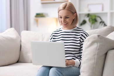 Photo of Happy middle aged woman using laptop on sofa at home