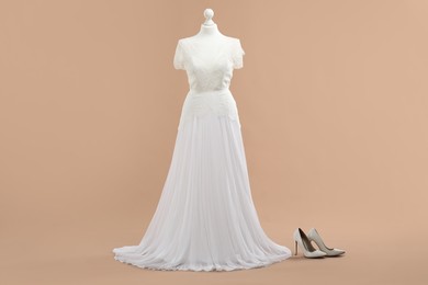 Photo of Mannequin with beautiful wedding dress and shoes on pale brown background