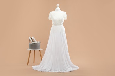 Photo of Mannequin with beautiful wedding dress and shoes on pale brown background