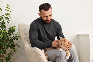 Man petting cute ginger cat on armchair at home