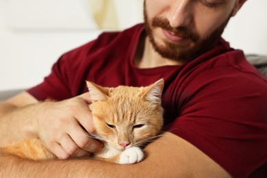 Man petting cute ginger cat on armchair at home, closeup