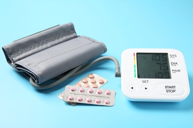 Photo of Blood pressure measuring device and pill blisters on light blue background