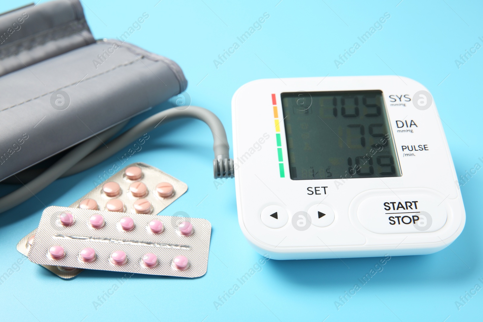 Photo of Blood pressure measuring device and pill blisters on light blue background