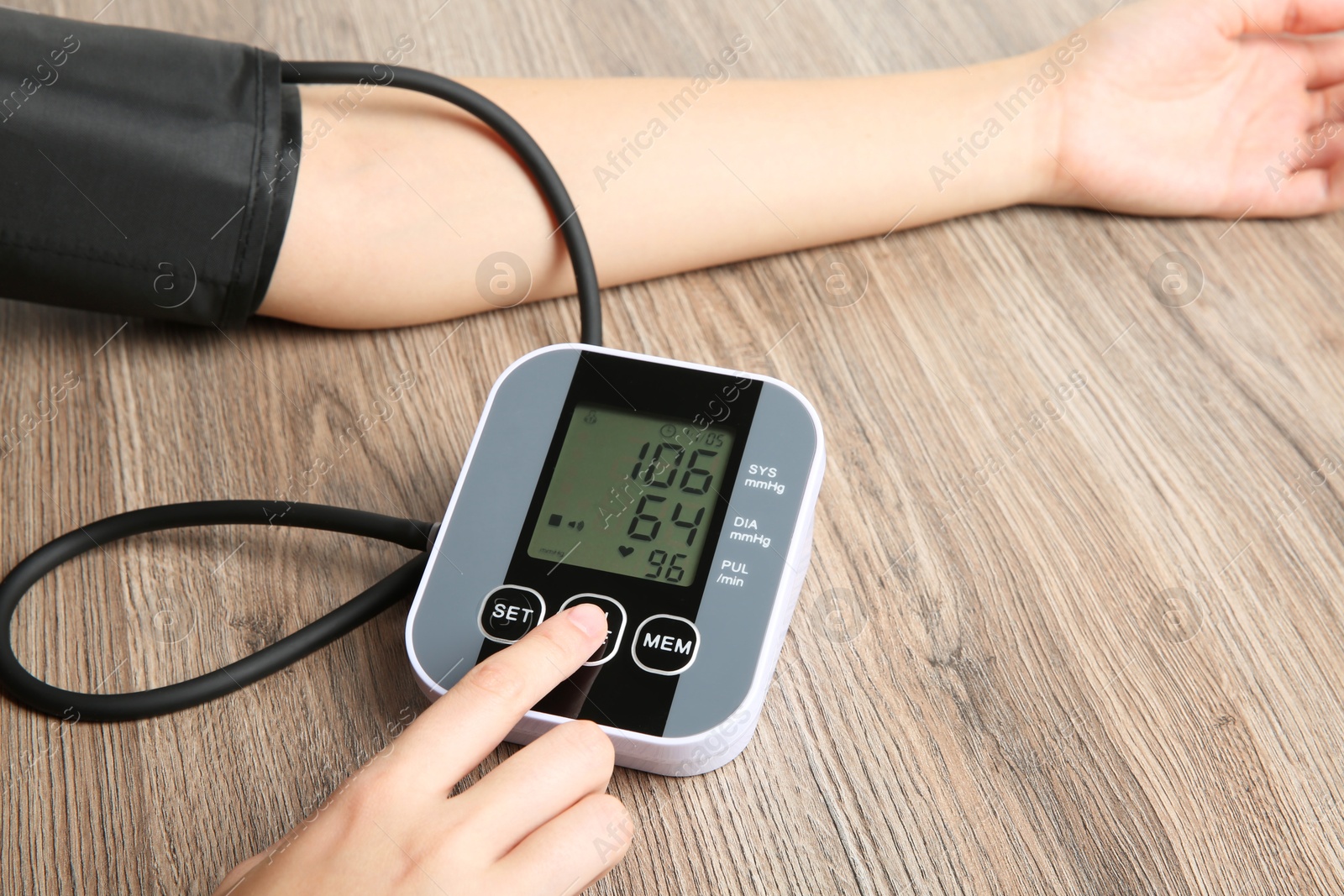 Photo of Woman measuring her blood pressure with device at wooden table, closeup