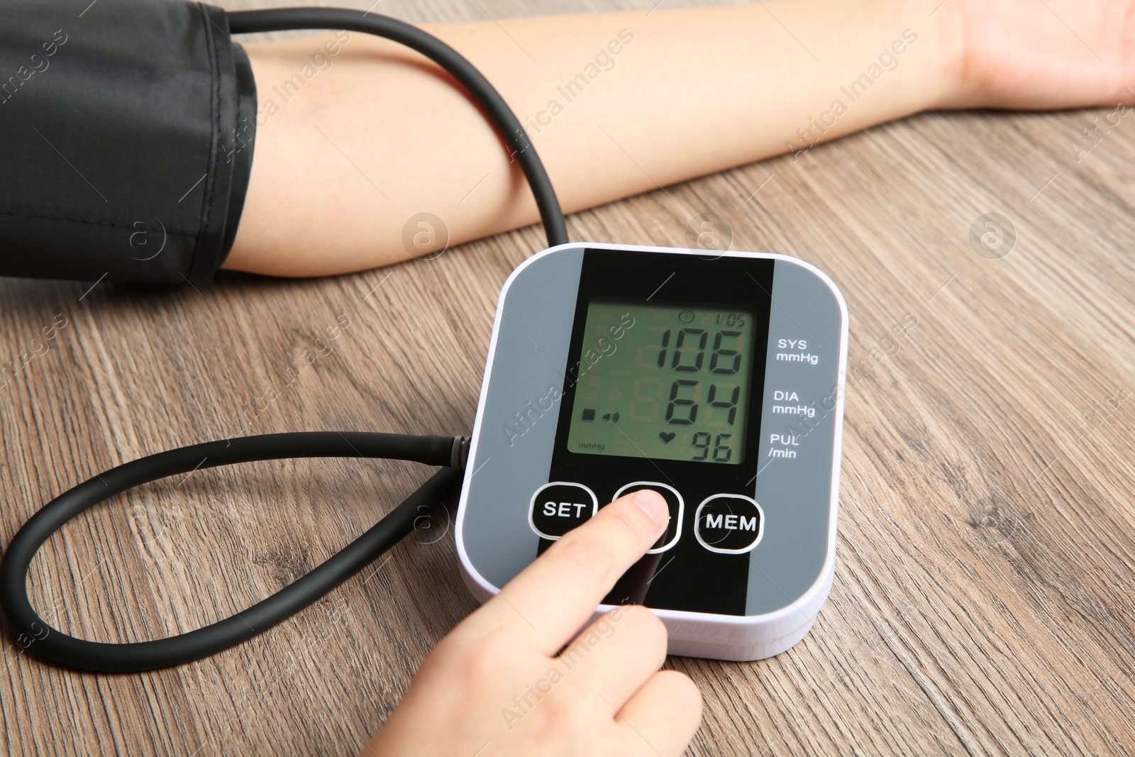 Photo of Woman measuring her blood pressure with device at wooden table, closeup