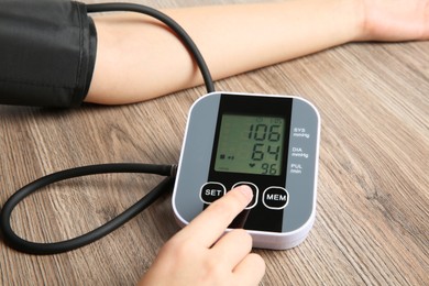 Photo of Woman measuring her blood pressure with device at wooden table, closeup