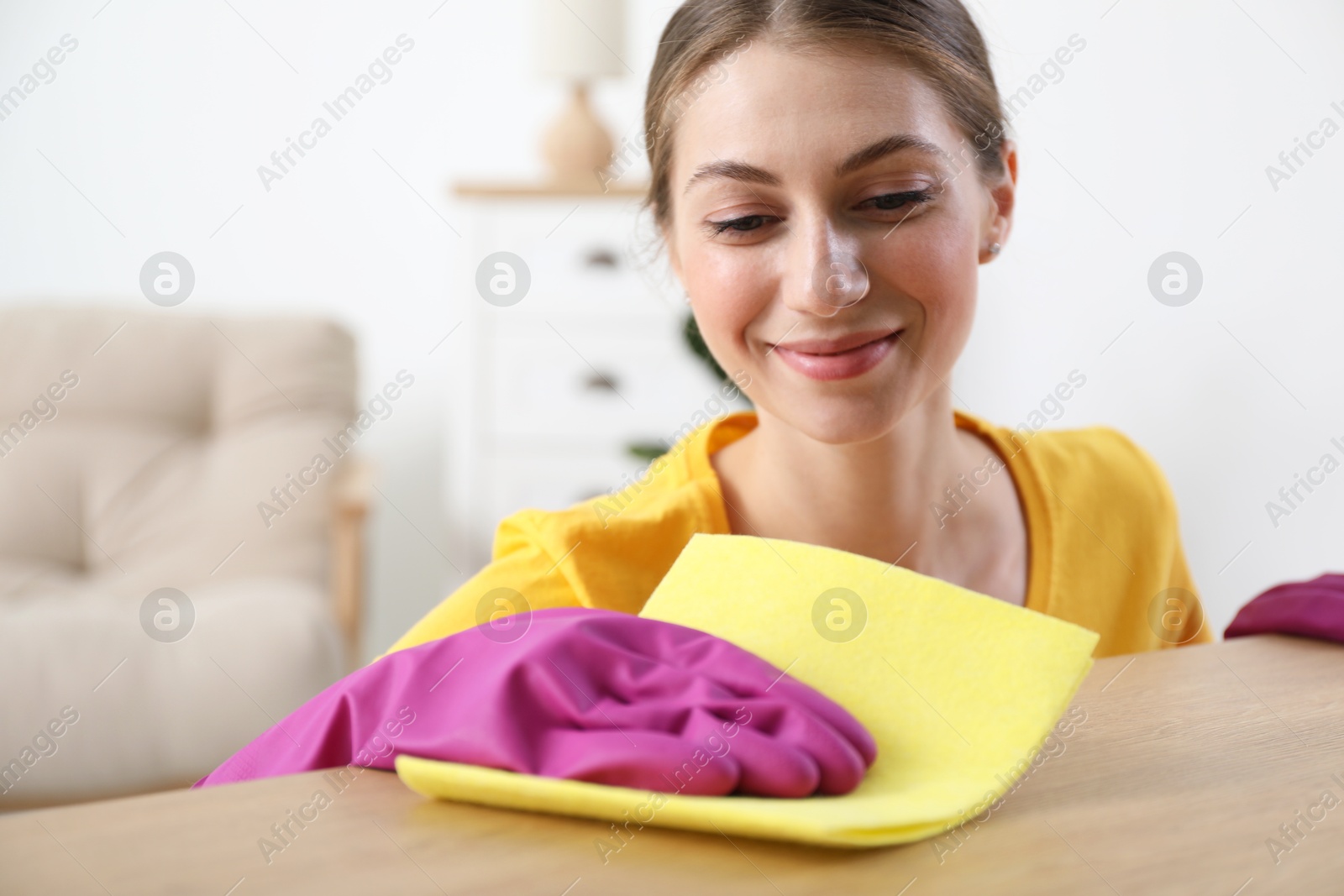 Photo of Young woman cleaning table with rag at home