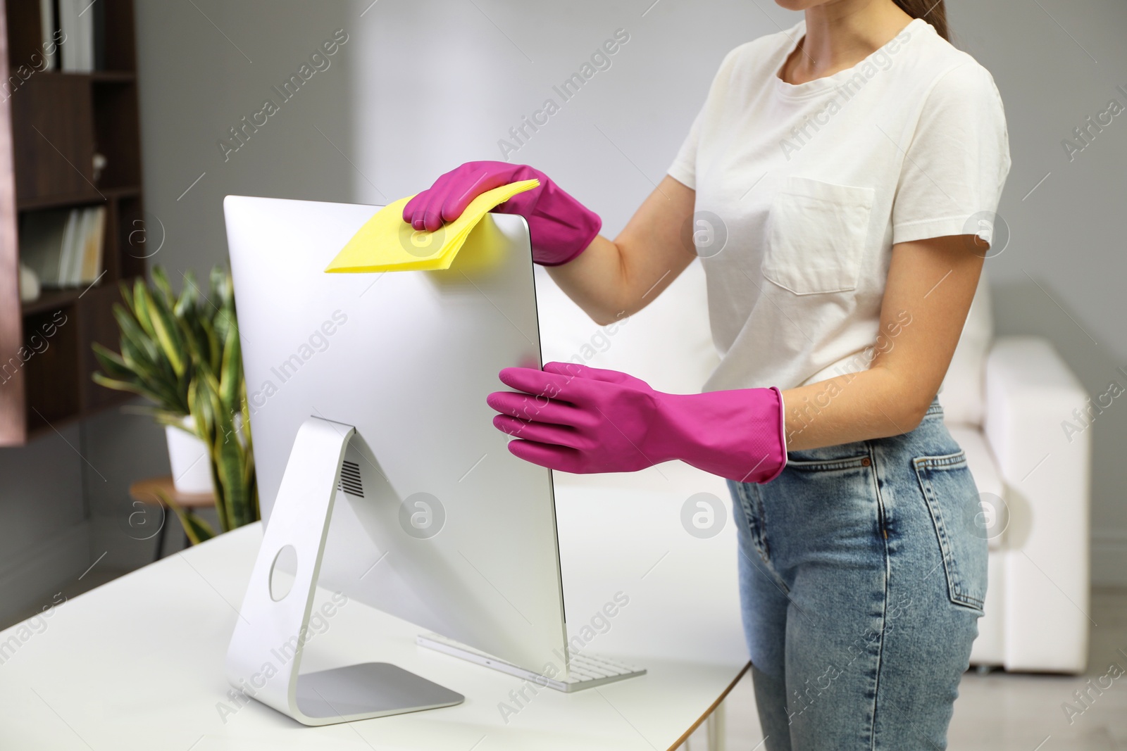 Photo of Young woman cleaning computer with rag and spray in office, closeup