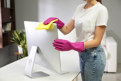 Young woman cleaning computer with rag and spray in office, closeup