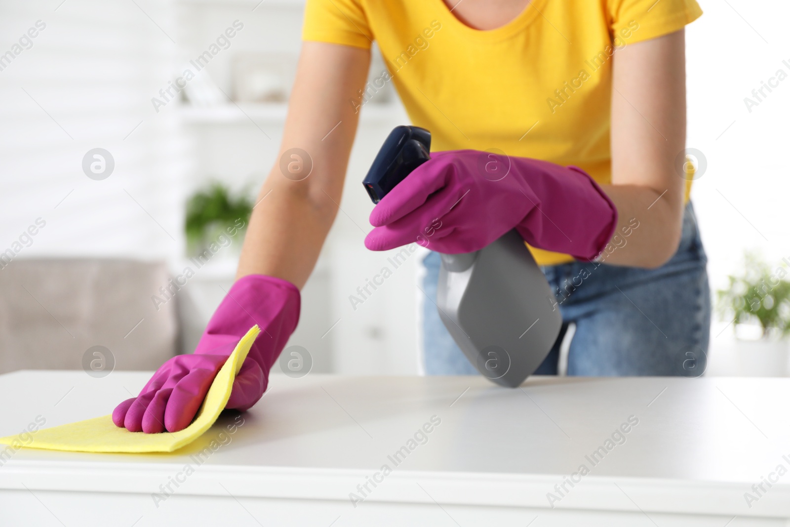 Photo of Young woman cleaning table with rag and spray in office, closeup