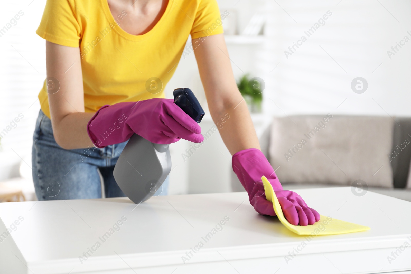 Photo of Young woman cleaning table with rag and spray in office, closeup