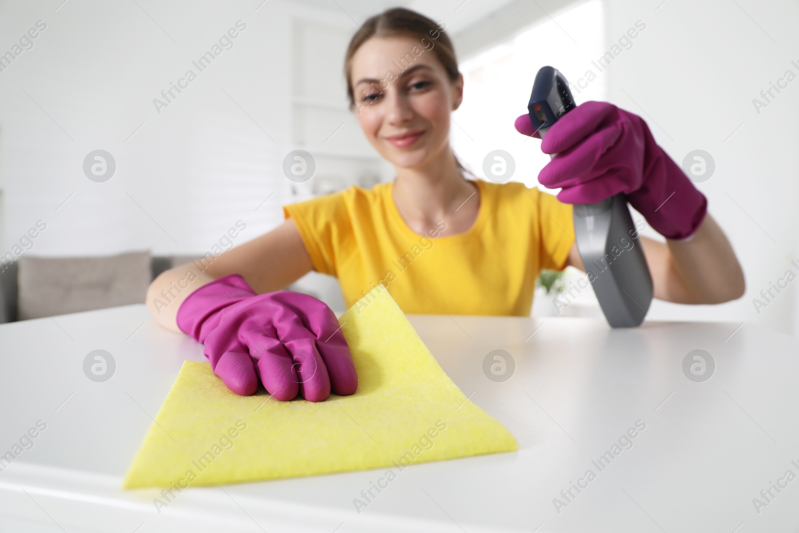 Photo of Young woman cleaning table with rag and spray in office, selective focus